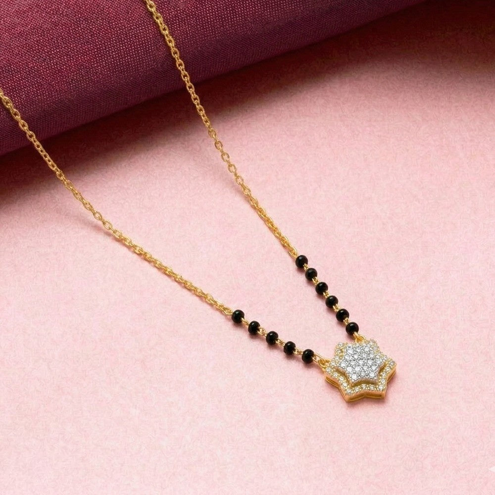 A gold and diamond mangalsutra featuring a beaded section with small black beads and a gold paved with clear stones, displayed on a pink background with a dark purple fabric accent.