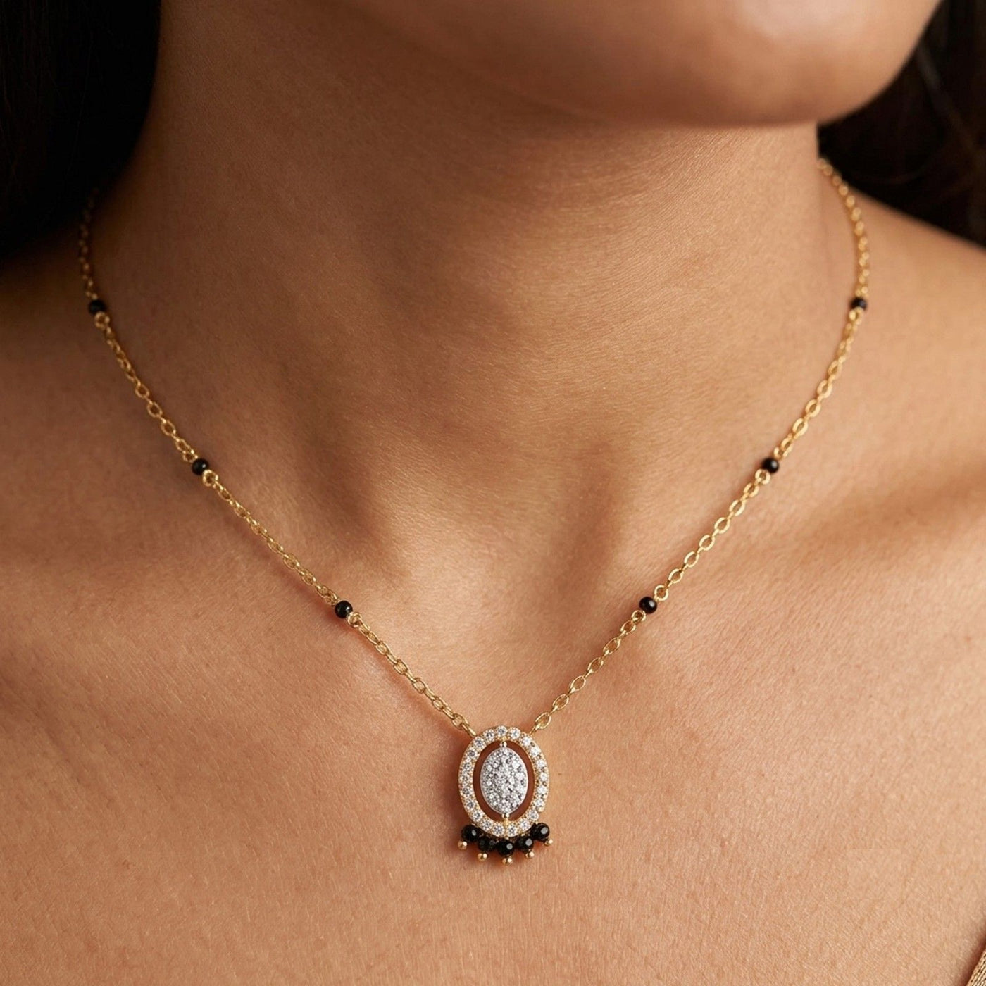 A close-up of a model's neck and chest wearing a delicate gold mangalsutra with a central oval pendant. 