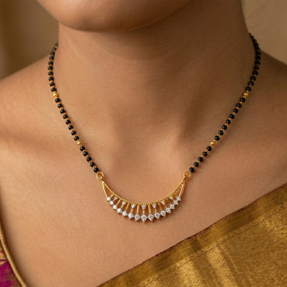 A close-up of a woman wearing a traditional Indian mangalsutra featuring a gold crescent with small clear stones and black beads on a gold chain.