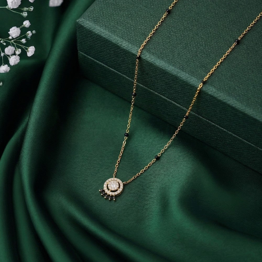 Gold and diamond mangalsutra with a diamond on a green fabric background
