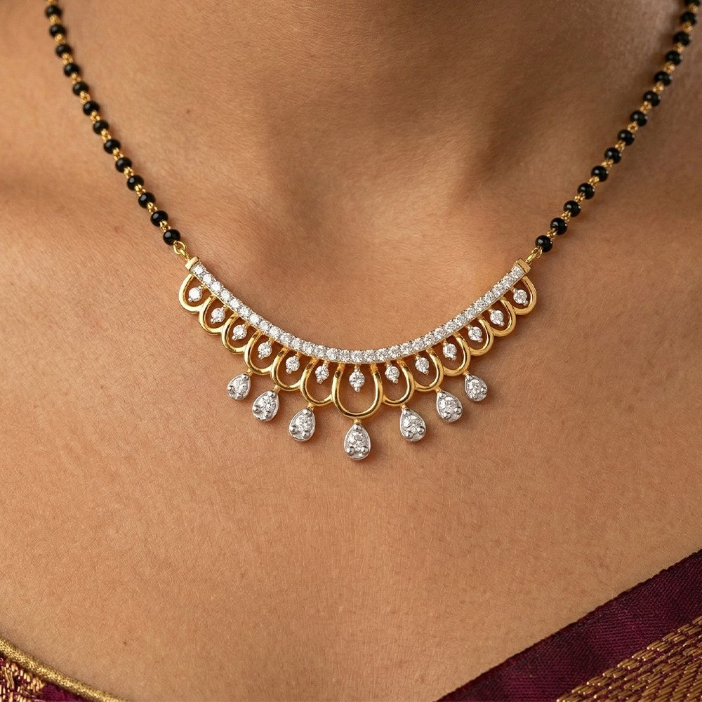 Gold and black beaded mangalsutra with diamond-like stones on a person wearing a saree.