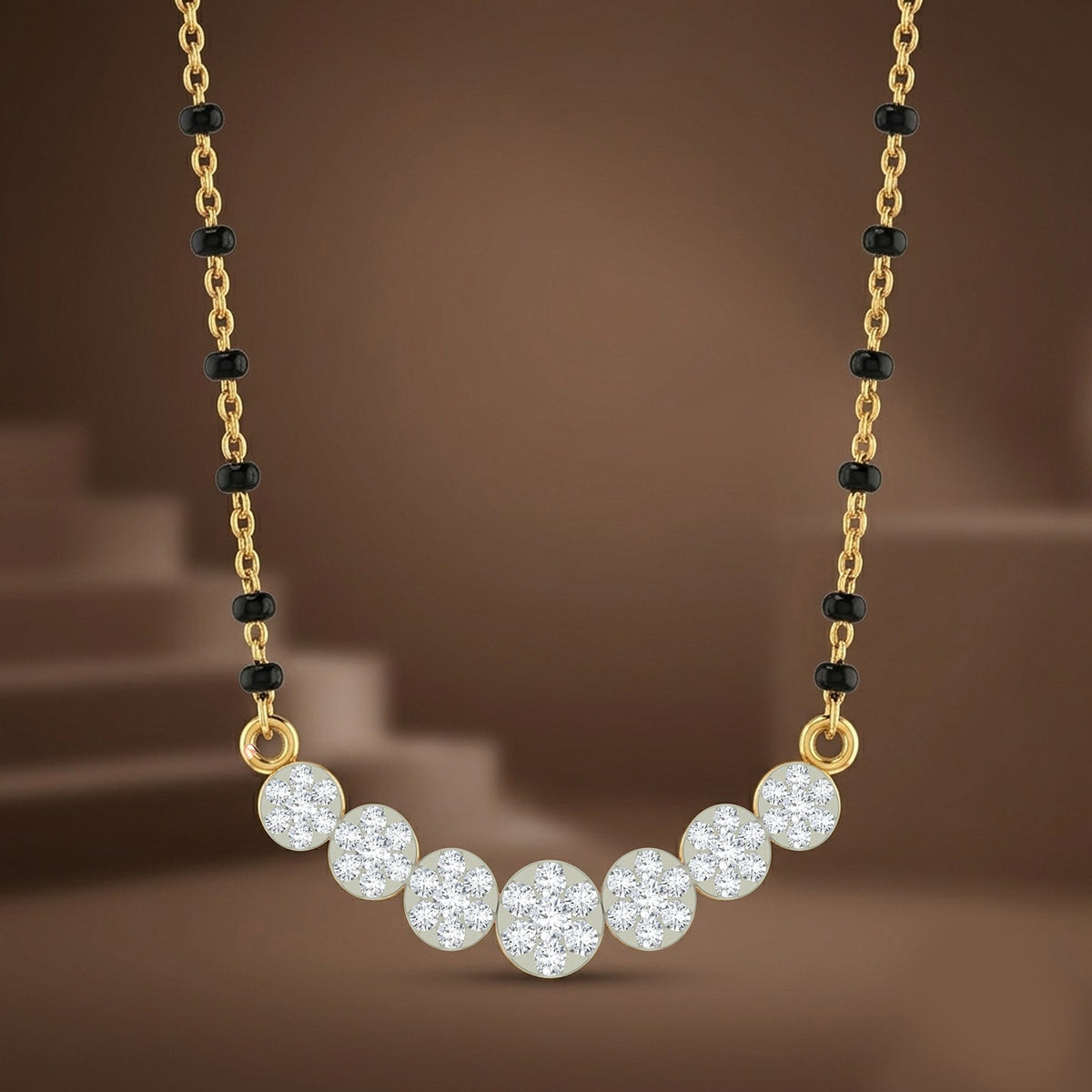 A gold mangalsutra featuring a curved row of seven clear, sparkling round gemstones in a gold setting, accented by small black beads along the chain, set against a warm brown background.