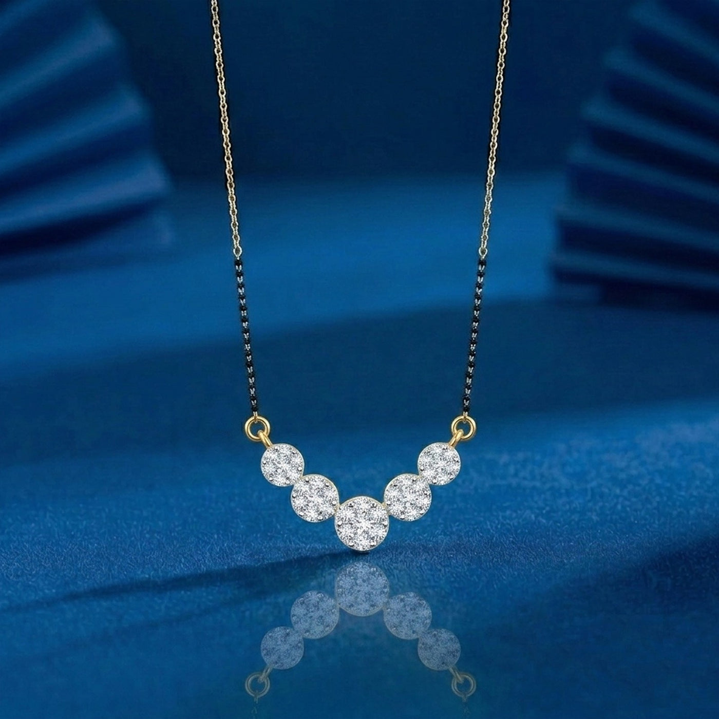 A delicate mangalsutra with five clear round-cut stones set in a curved row on a fine gold-toned chain, displayed against a deep blue reflective background.