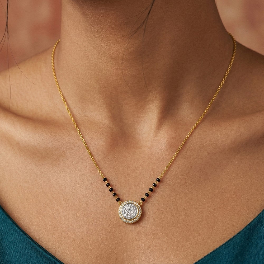 Gold and diamond mangalsutra with a round pendant on a person wearing a teal top.