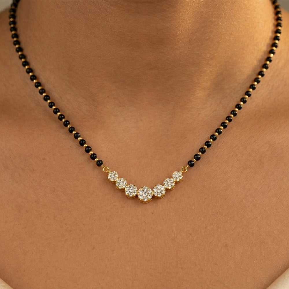 gold and diamond mangalsutra with black beads and a gold and diamond clasp on a person's neck.