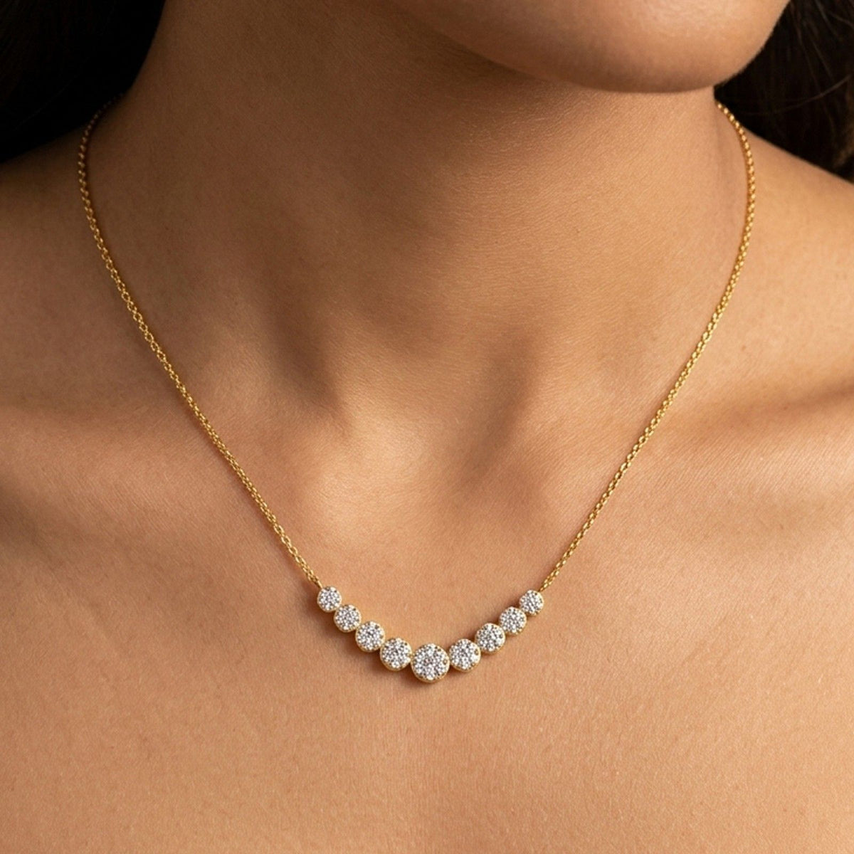 A close-up of a model's neck and upper chest wearing a delicate gold chain mangalsutra with a curved row of sparkling clear stones in a halo setting.