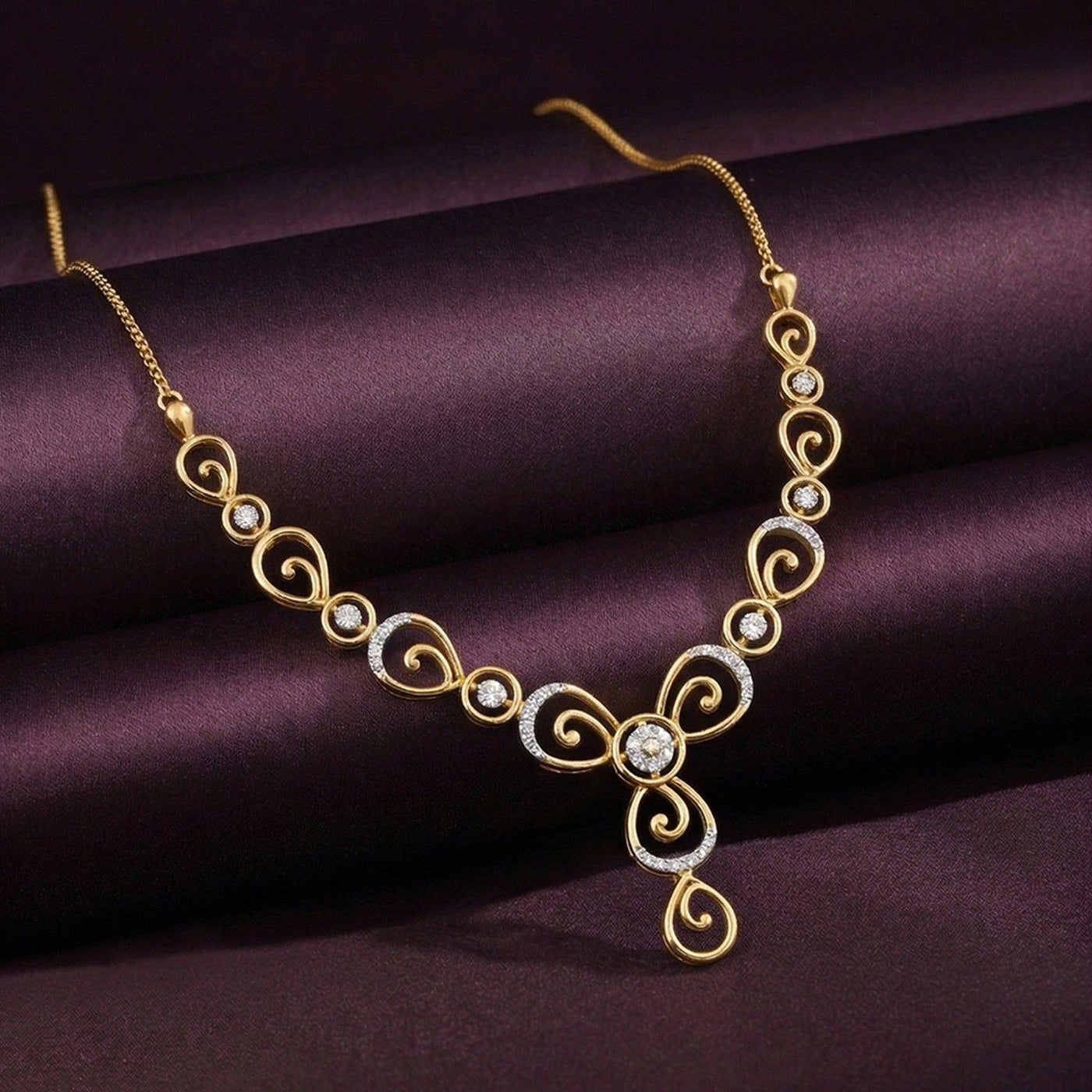 Gold necklace featuring intricate scrollwork and diamond-encrusted accents, displayed on a dark purple satin surface.