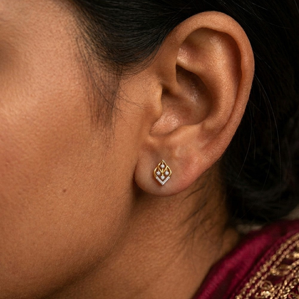 A close-up of a person's ear wearing gold and diamond stud earring.