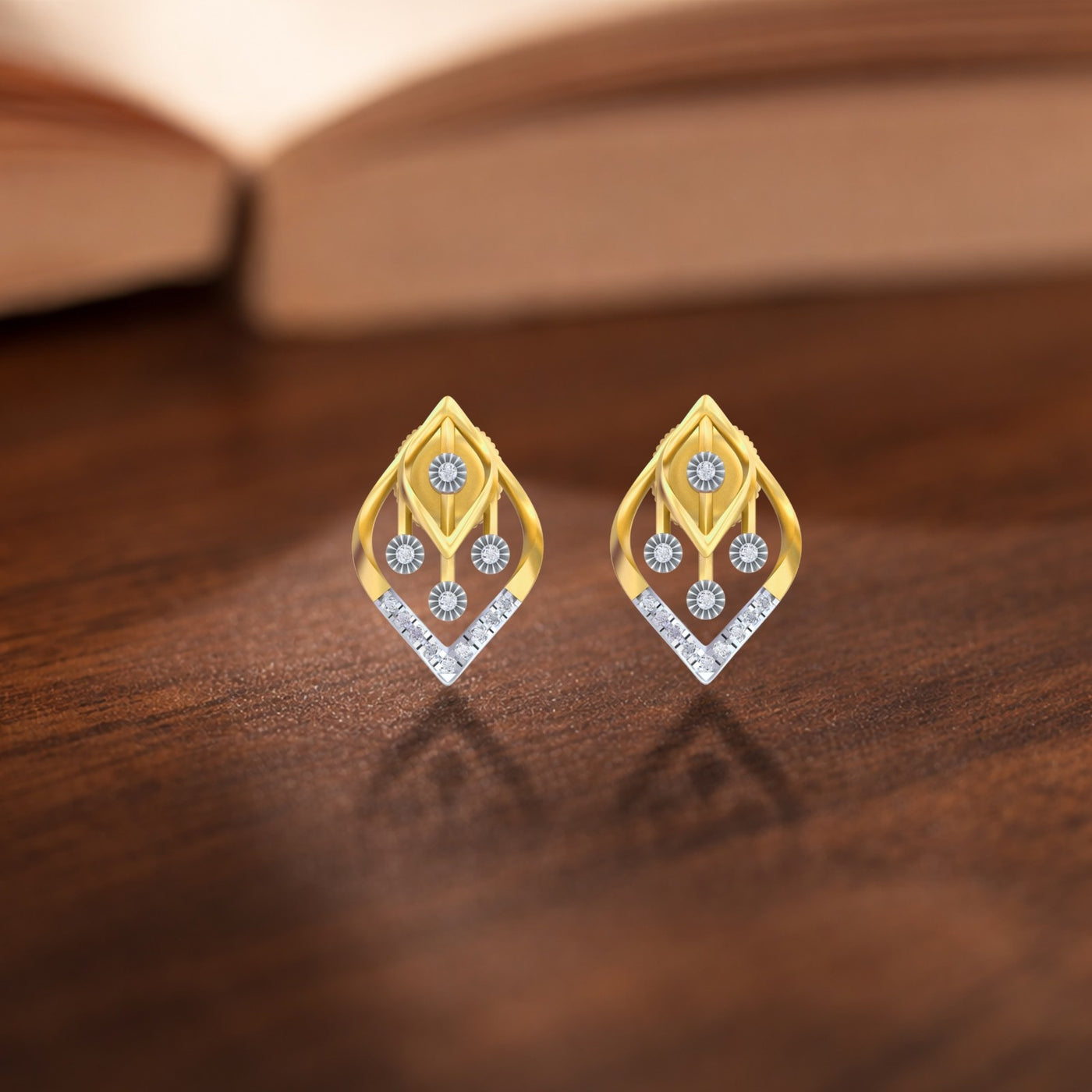 Gold and diamond earrings with marquise designs on a wooden surface.