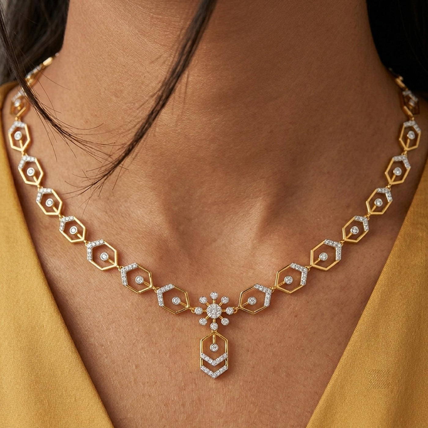 A close-up of a woman wearing a gold geometric necklace and features repeating hexagonal links and a central floral motif.