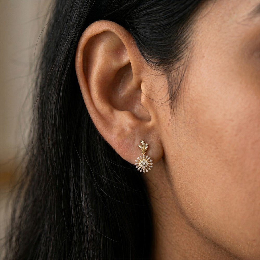 A close-up of a person's ear wearing a gold dangle earring with a sunburst or flower-like design earrings.