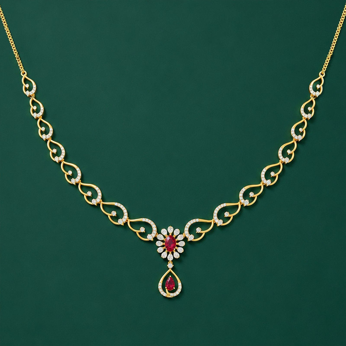Gold and diamond necklace with a floral and teardrop pendant design, featuring ruby gemstones, displayed against a solid dark green background.