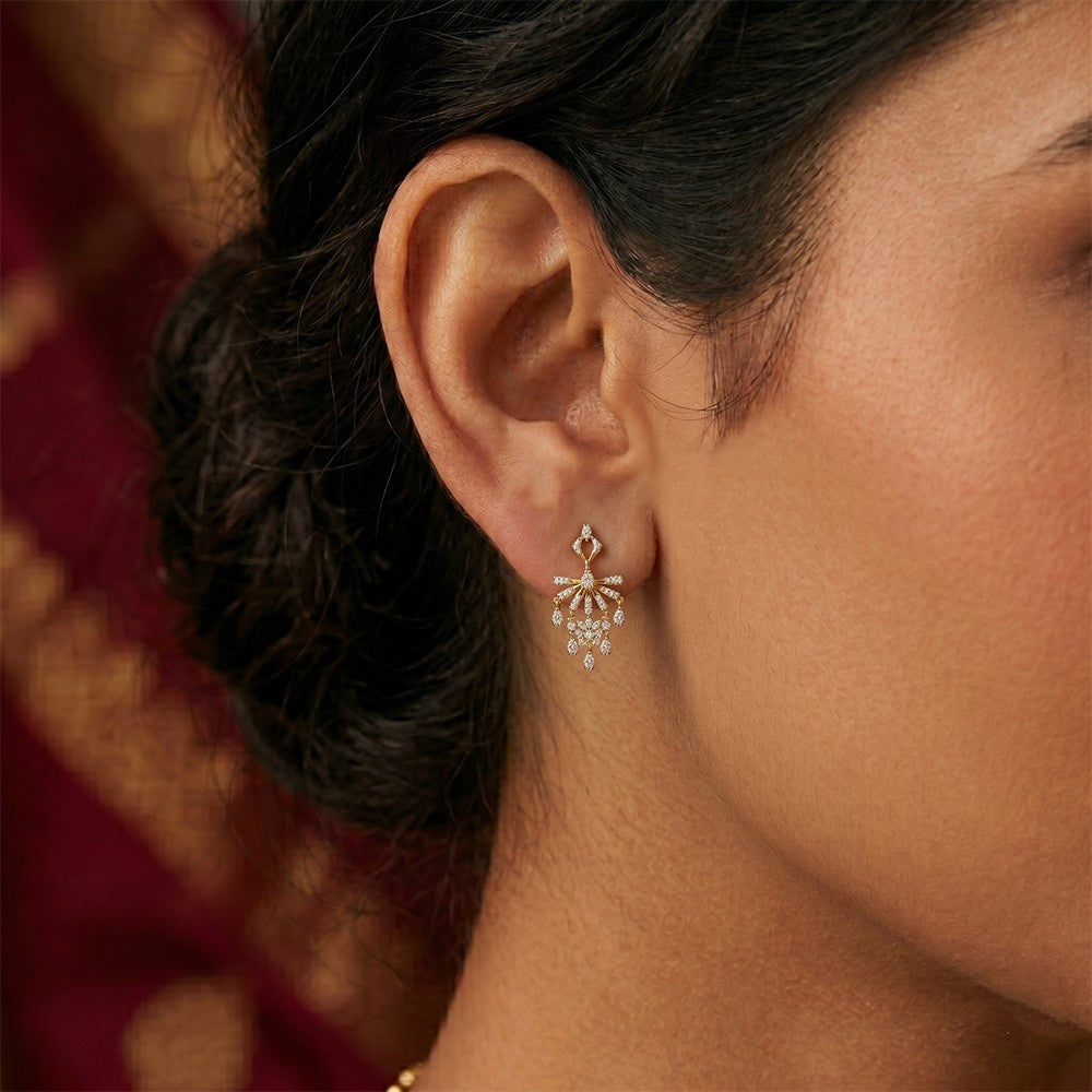A close-up of a woman's ear wearing a gold and diamond drop earring.