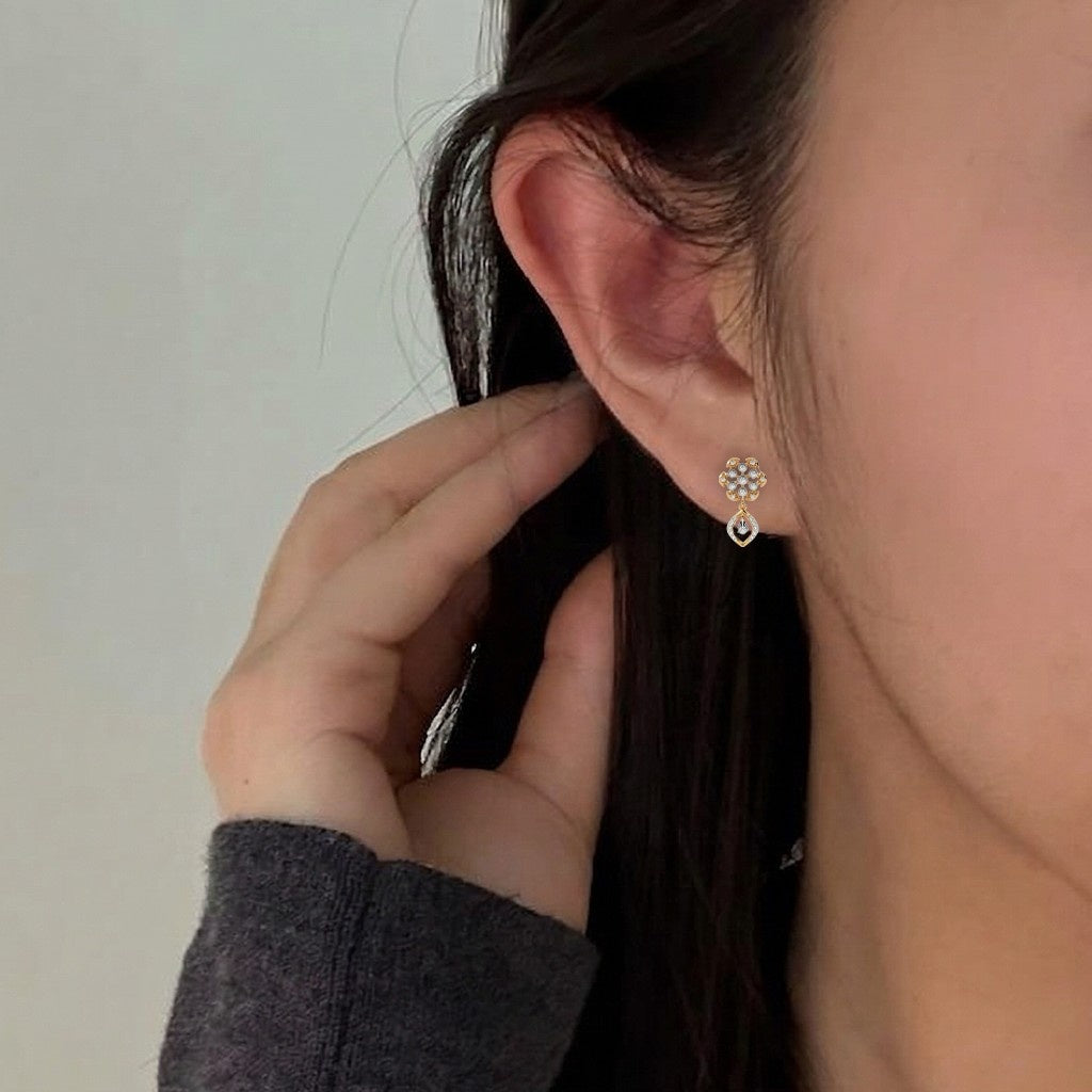 A close-up of a person's ear wearing a gold earrings with diamond accents in an elegant floral and teardrop design.
