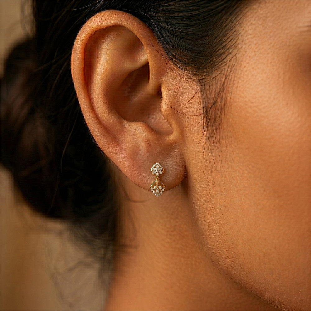 A close-up of a person's ear wearing gold earrings with diamond accents, featuring a floral and geometric pattern.