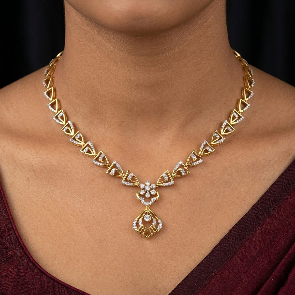 A close-up of a woman wearing a gold and diamond necklace with a geometric pattern and a teardrop.