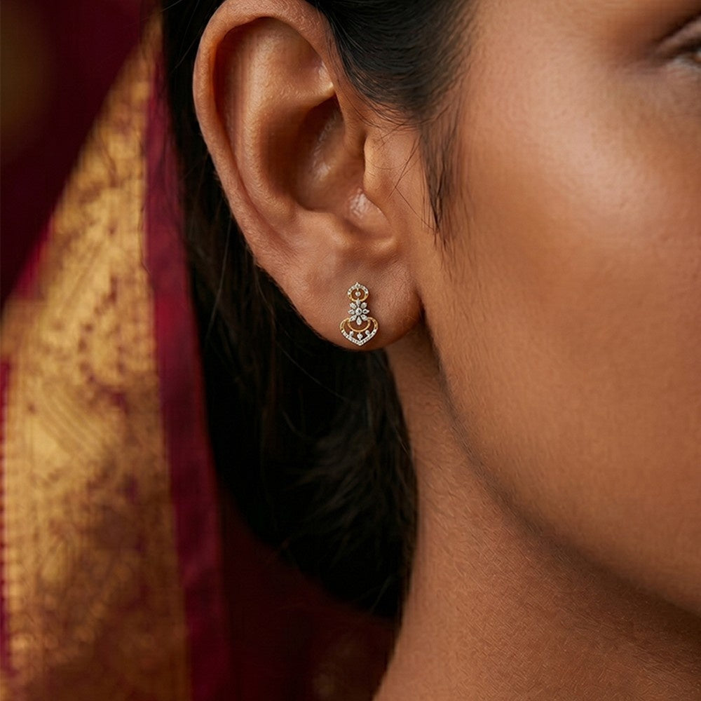 A close-up of a woman's ear wearing a gold and diamond earrings, featuring a heart-shaped design with floral and circular details.
