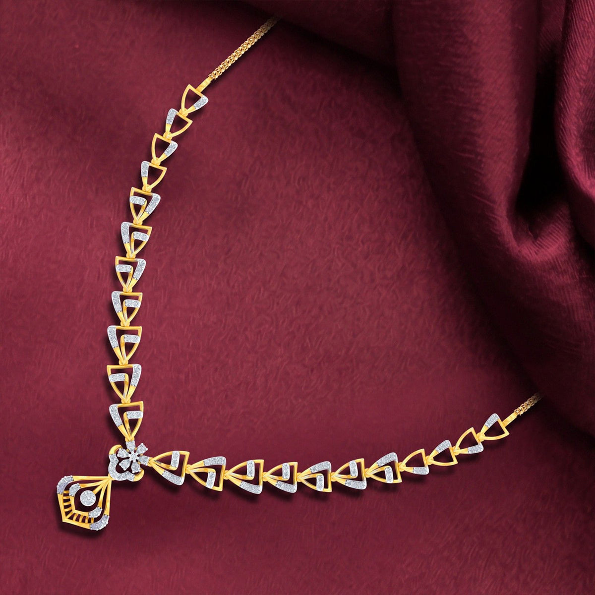 Gold and diamond geometric necklace with a central floral motif, displayed on a draped burgundy fabric background.