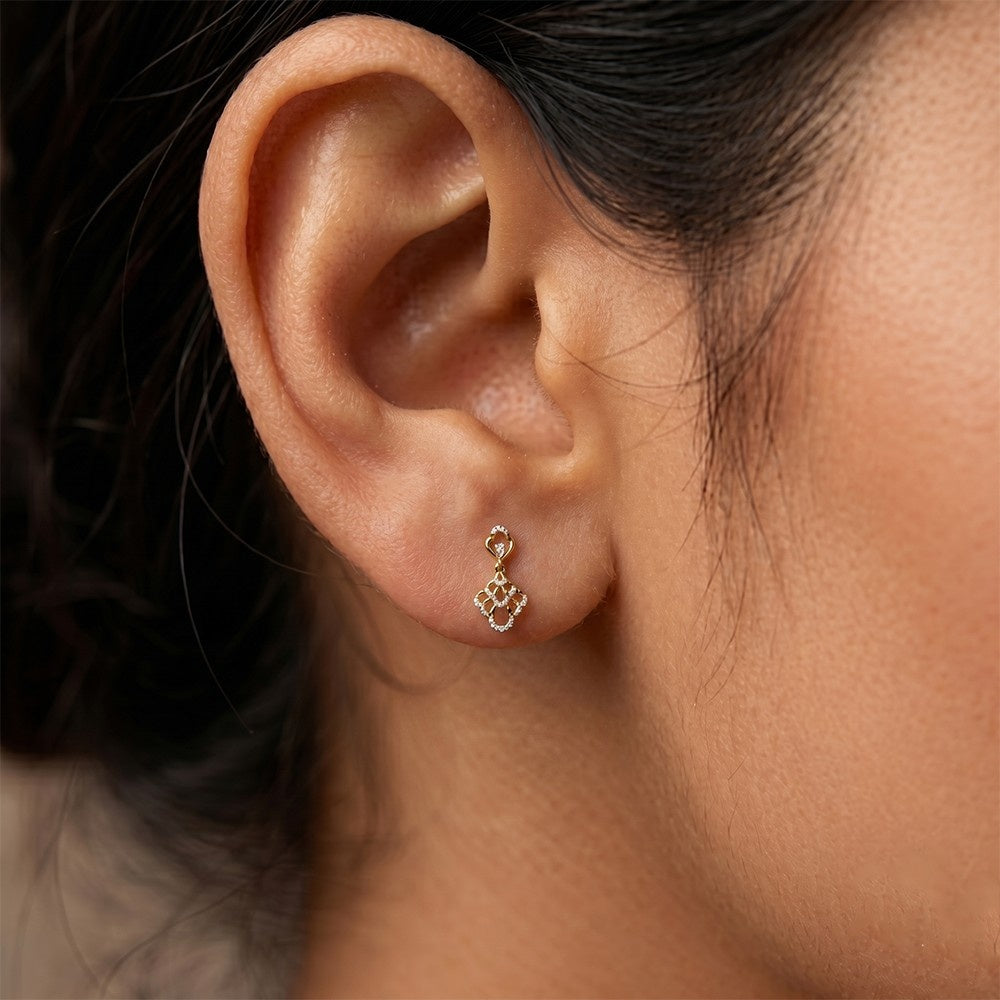 A close-up of a person's ear wearing a gold earrings with sparkling diamond accents.
