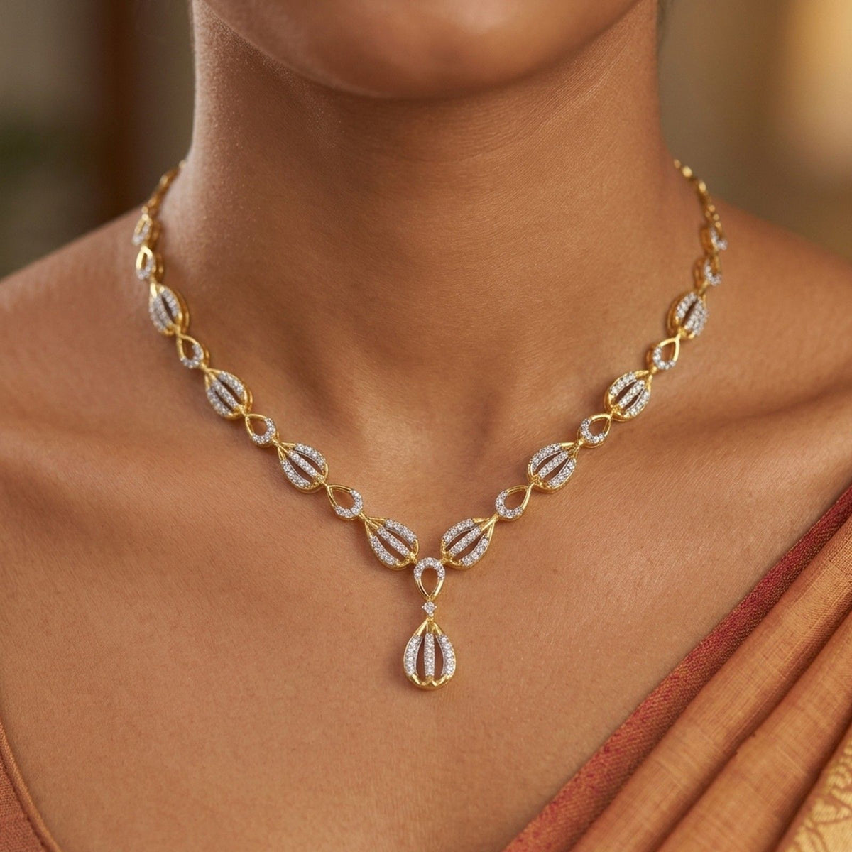 A gold necklace with diamond-encrusted leaf and teardrop motifs, shown worn on a model's neck against a softly blurred warm background.