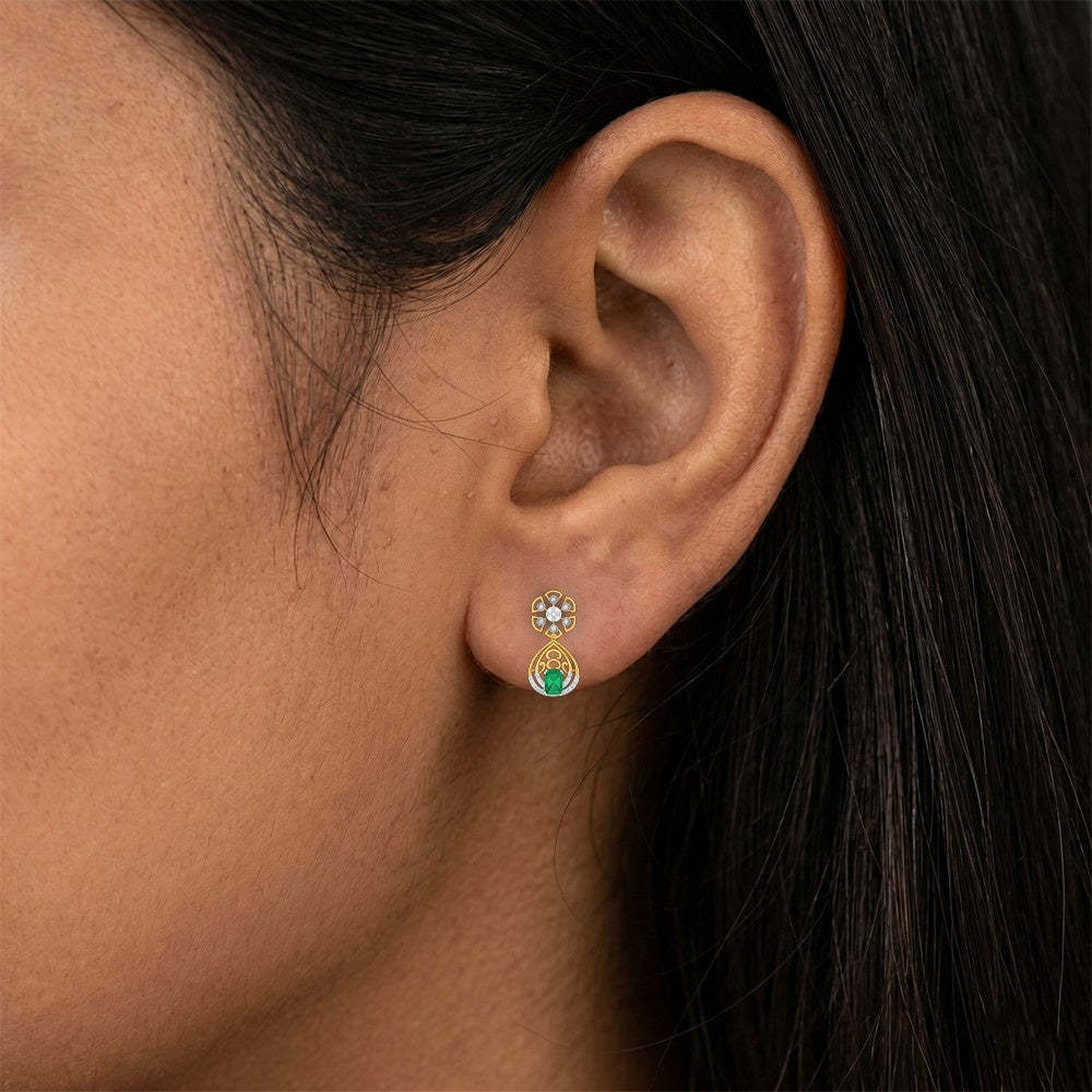 A close-up of a person's ear wearing a gold and diamond earrings with green gemstones.