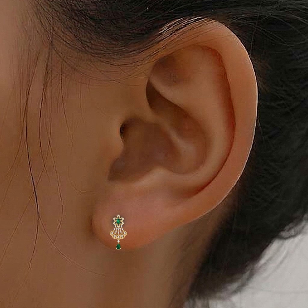 A close-up of a person's ear wearing a gold earring with green teardrop accent.