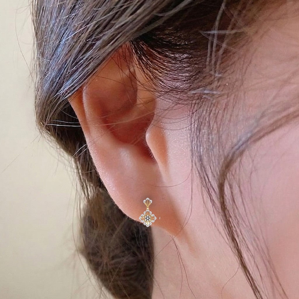 A close-up of a person's ear wearing a gold and diamond floral-shaped earrings.