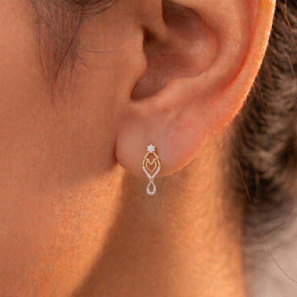 A close-up of a person's ear wearing a gold and diamond drop earrings.