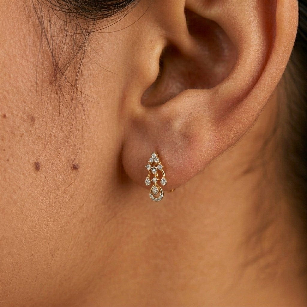A close-up of a person's ear wearing a gold and diamond drop earring.