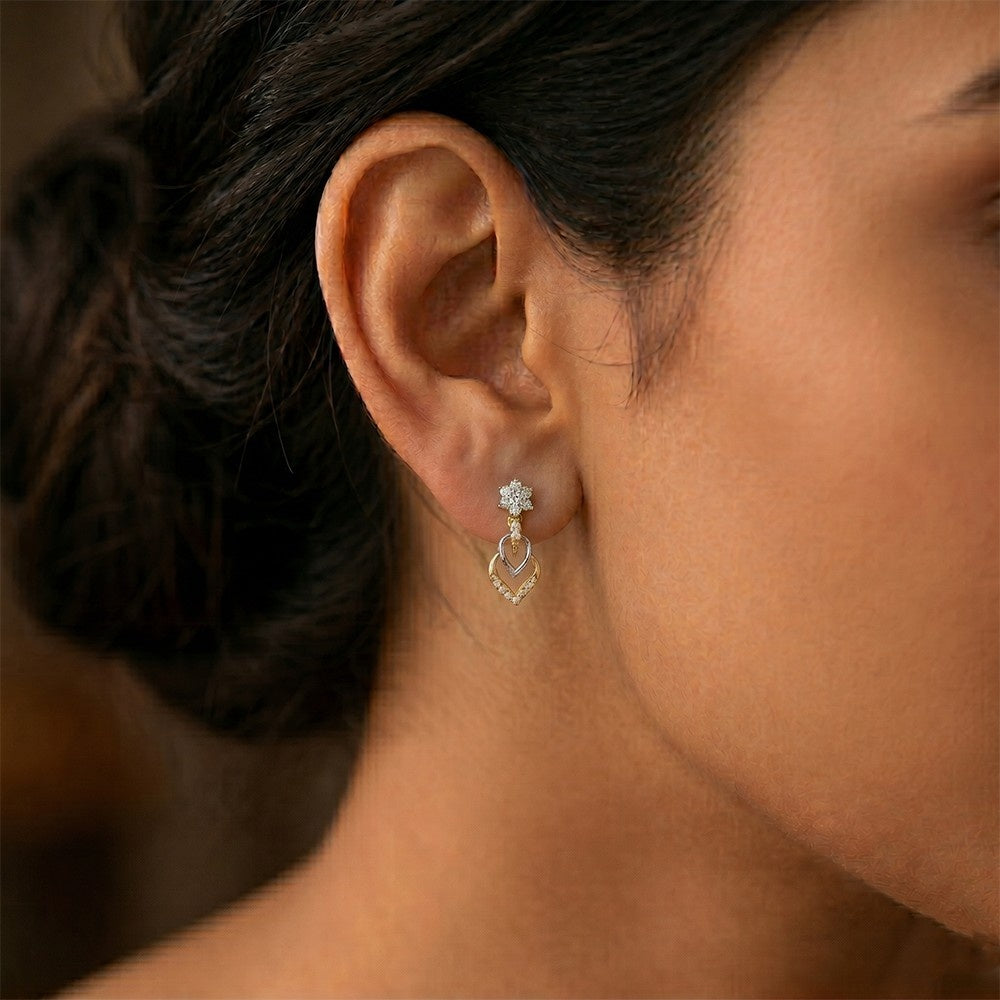 A close-up of a woman's ear wearing a gold dangle earring with floral stud earring.