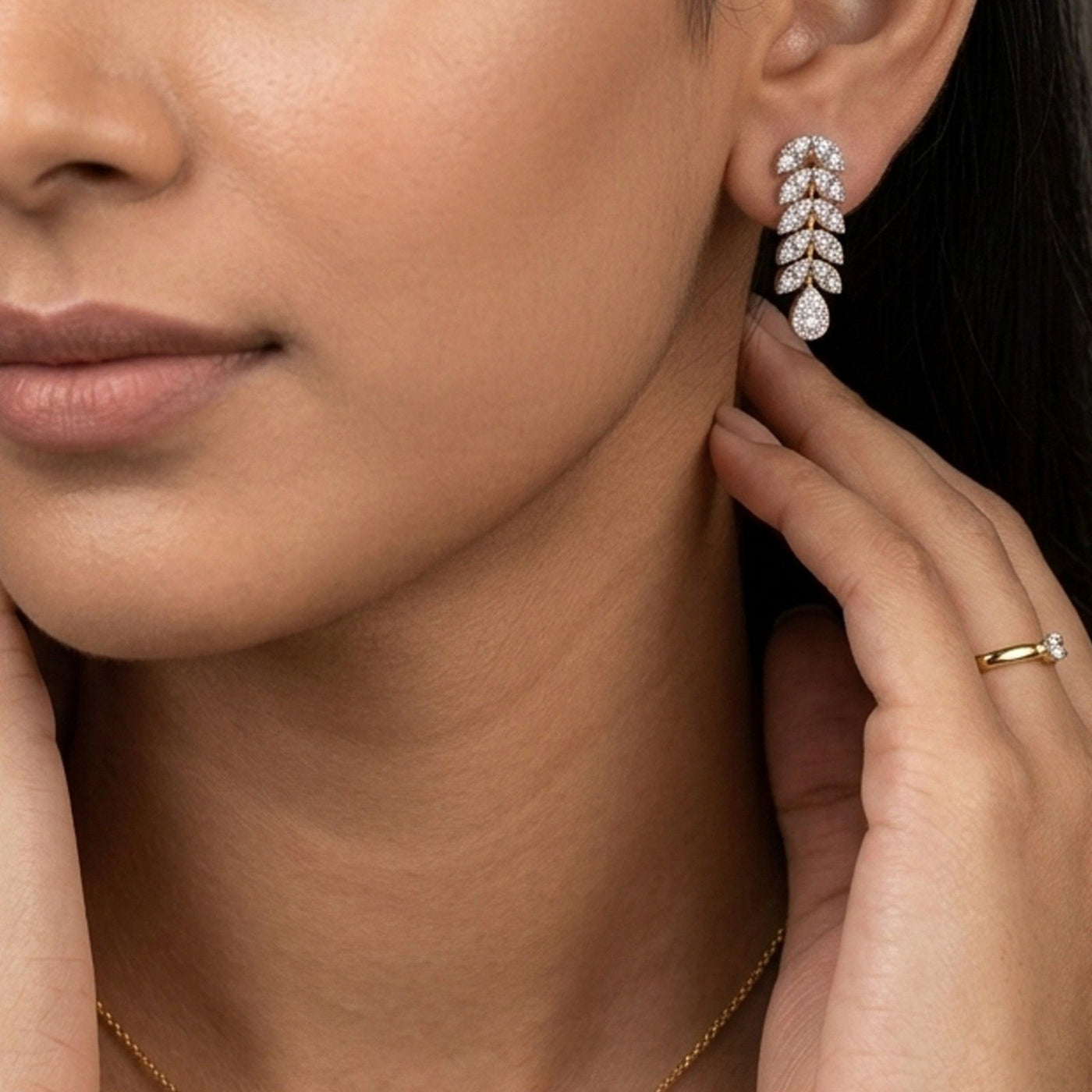 A close-up of a person's ear wearing a  gold earrings with leaf-like design and embedded diamonds.