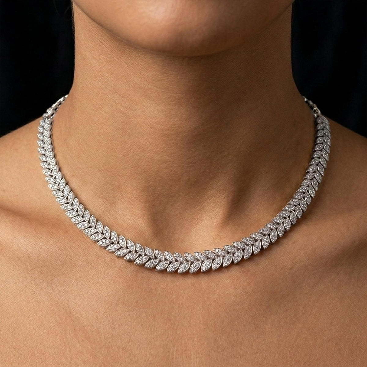 Gold necklace with leaf-design on a person's neck against a black background.