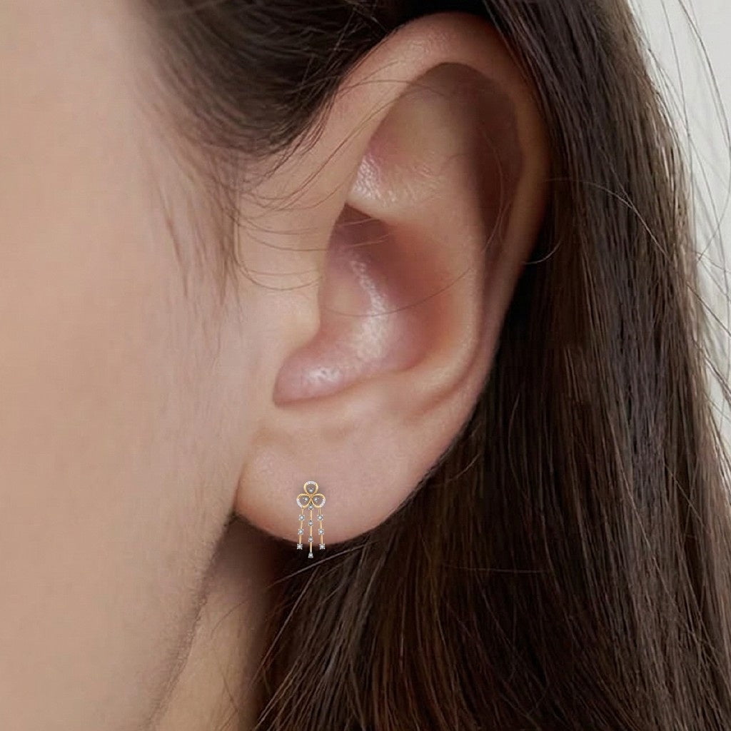 A close-up of a person's ear wearing a gold and diamond dangler earring with floral-shaped.