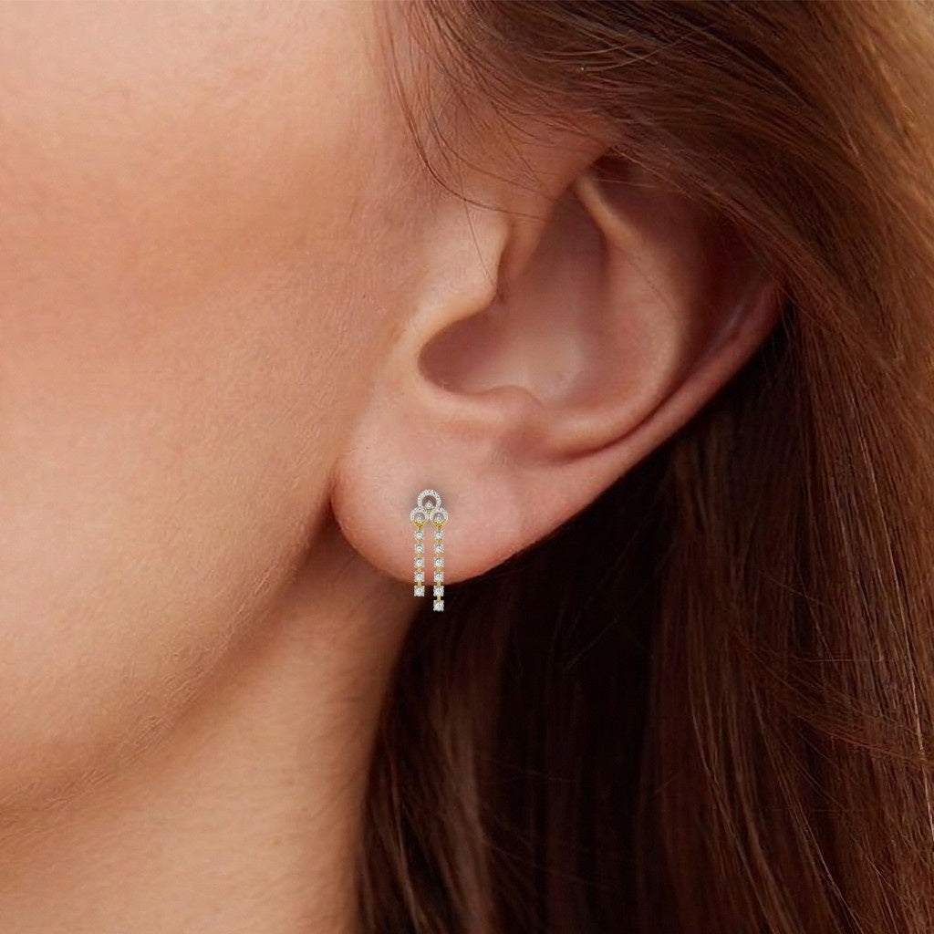 A close-up of a model's ear wearing a gold earrings with multiple diamond accents along the length of each earring, featuring a timeless design.
