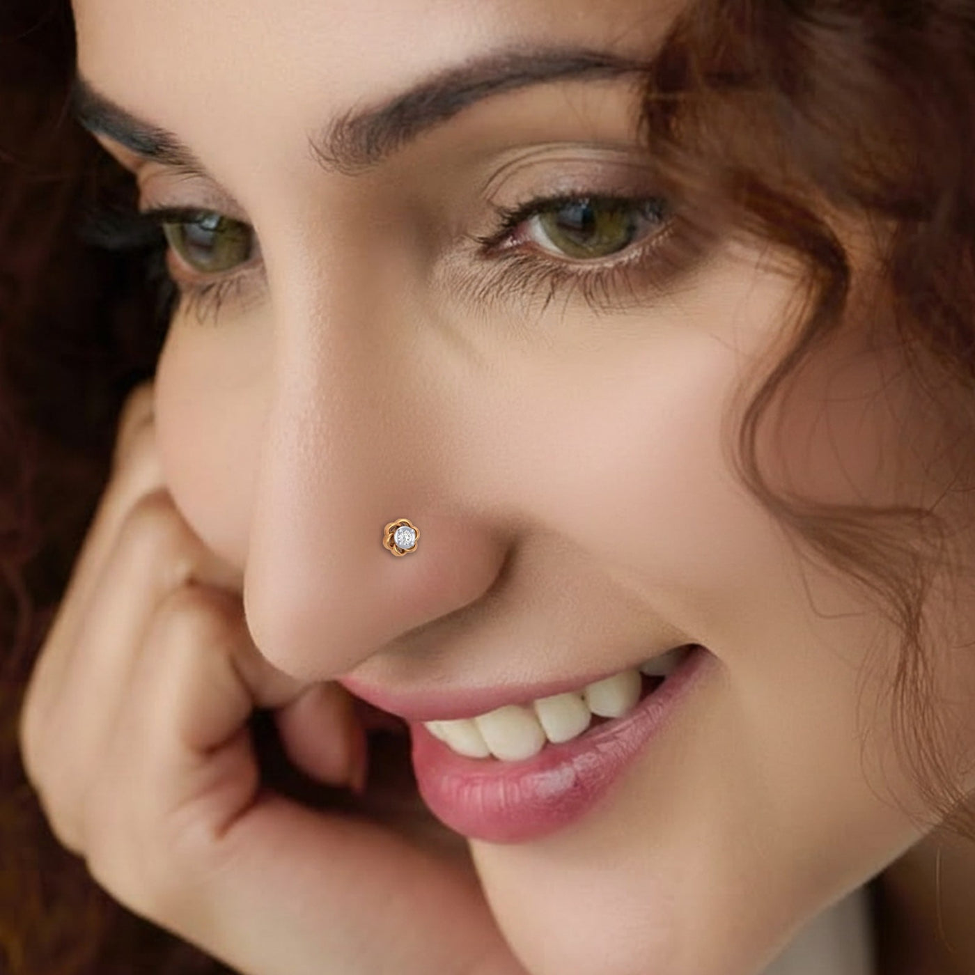 Close-up portrait of a smiling woman wearing a gold nose stud featuring a small round diamond center surrounded by a delicate, twisted gold swirl design on her nostril