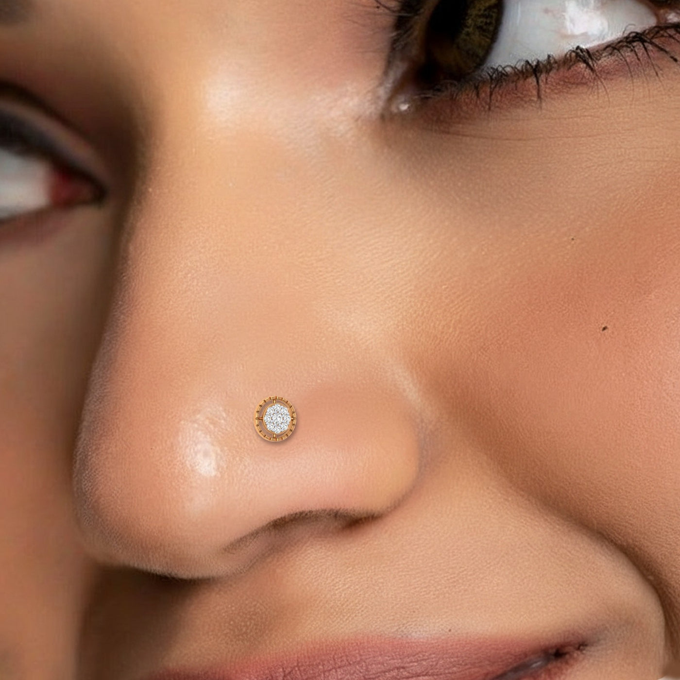 A close-up of a person's face wearing a small gold nose stud with clear rhinestones on the left side of the nose.