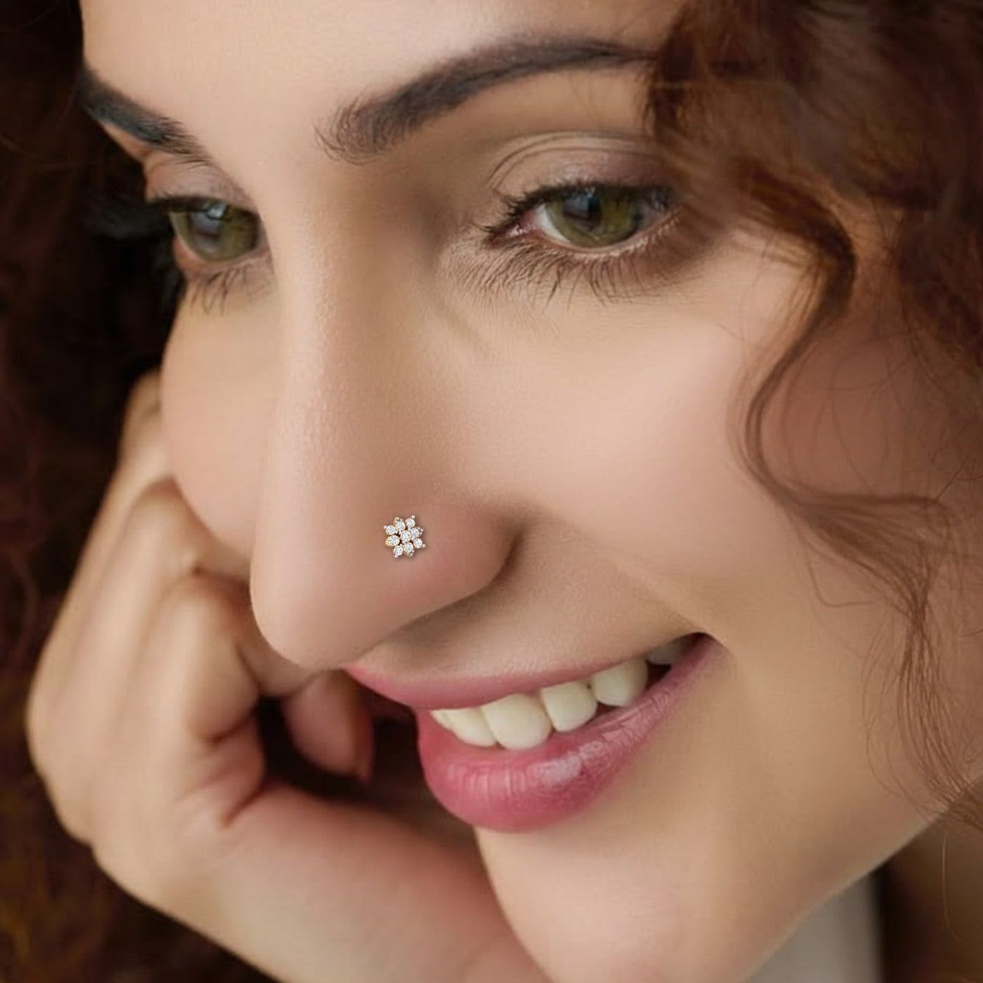 A close-up of a woman's face wearing a small, flower-shaped silver nose stud with a clear gemstone on her nose.
