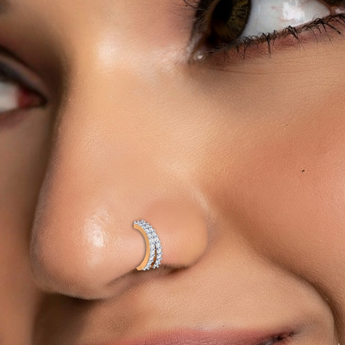 A close-up of a person's nose wearing a small silver-toned cross-shaped stud earring set with clear stones.