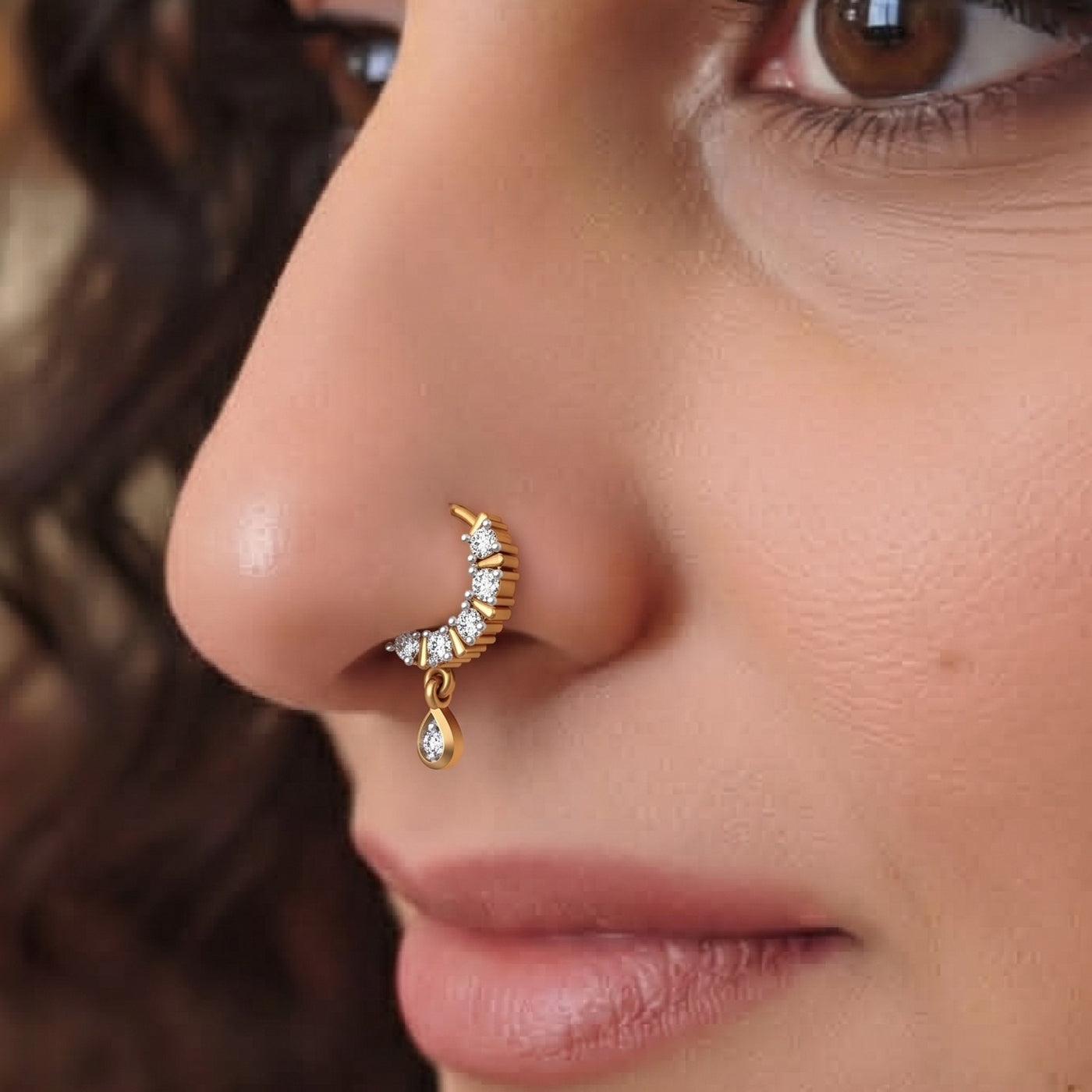 Close-up of a person's face highlighting an ornate gold nose ring in a crescent design set with small diamonds and featuring a dangling diamond-encrusted teardrop charm on the nostril.