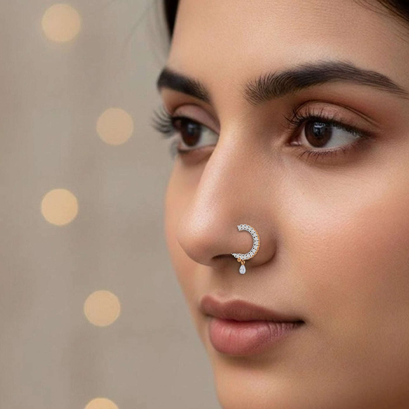 A close-up of a woman's face wearing a delicate gold crescent moon nose ring adorned with small clear stones 