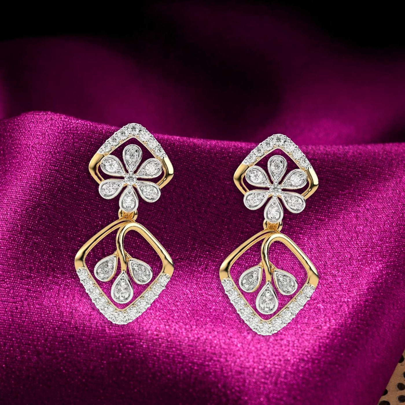 A pair of gold earrings with diamond accents, featuring a floral and geometric pattern on a magenta fabric background.