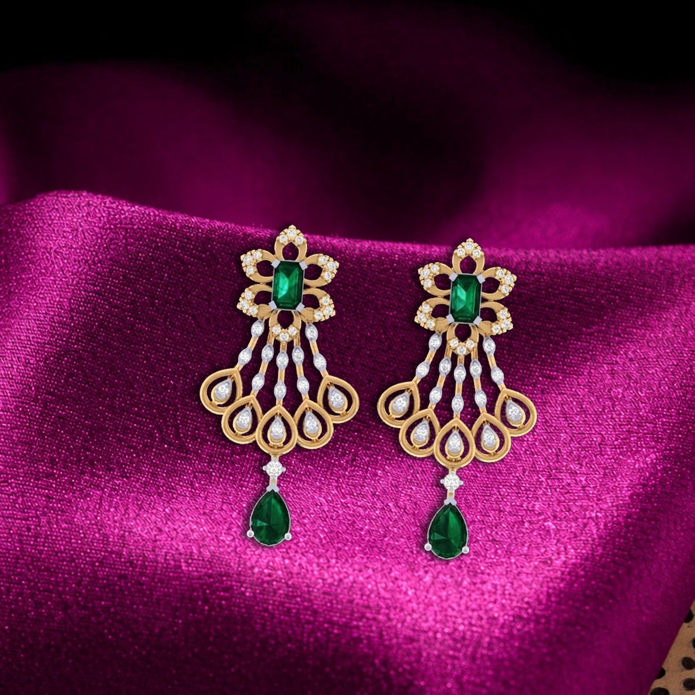 A pair of ornate gold, diamond, and green gemstone chandelier earrings displayed on a draped magenta fabric background