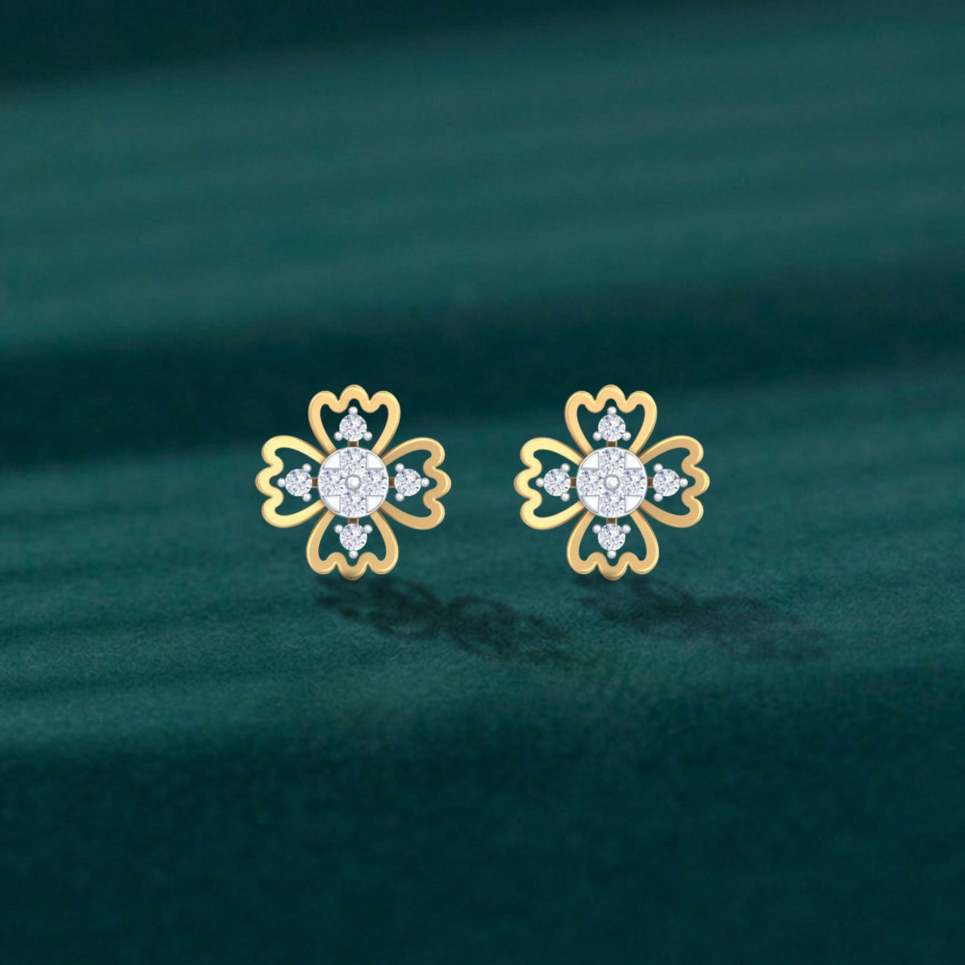 A pair of delicate gold and diamond floral stud earrings on a dark green velvet background