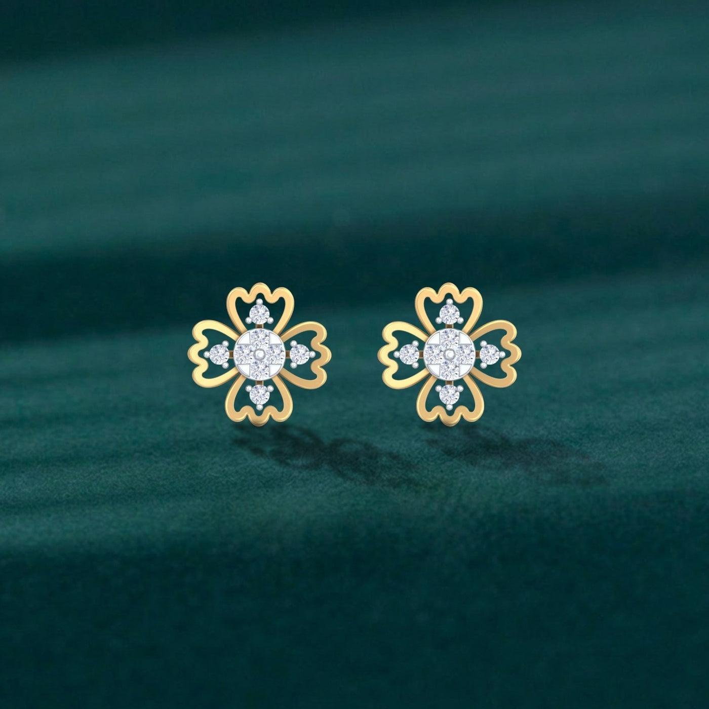 A pair of delicate gold and diamond floral stud earrings on a dark green velvet background.