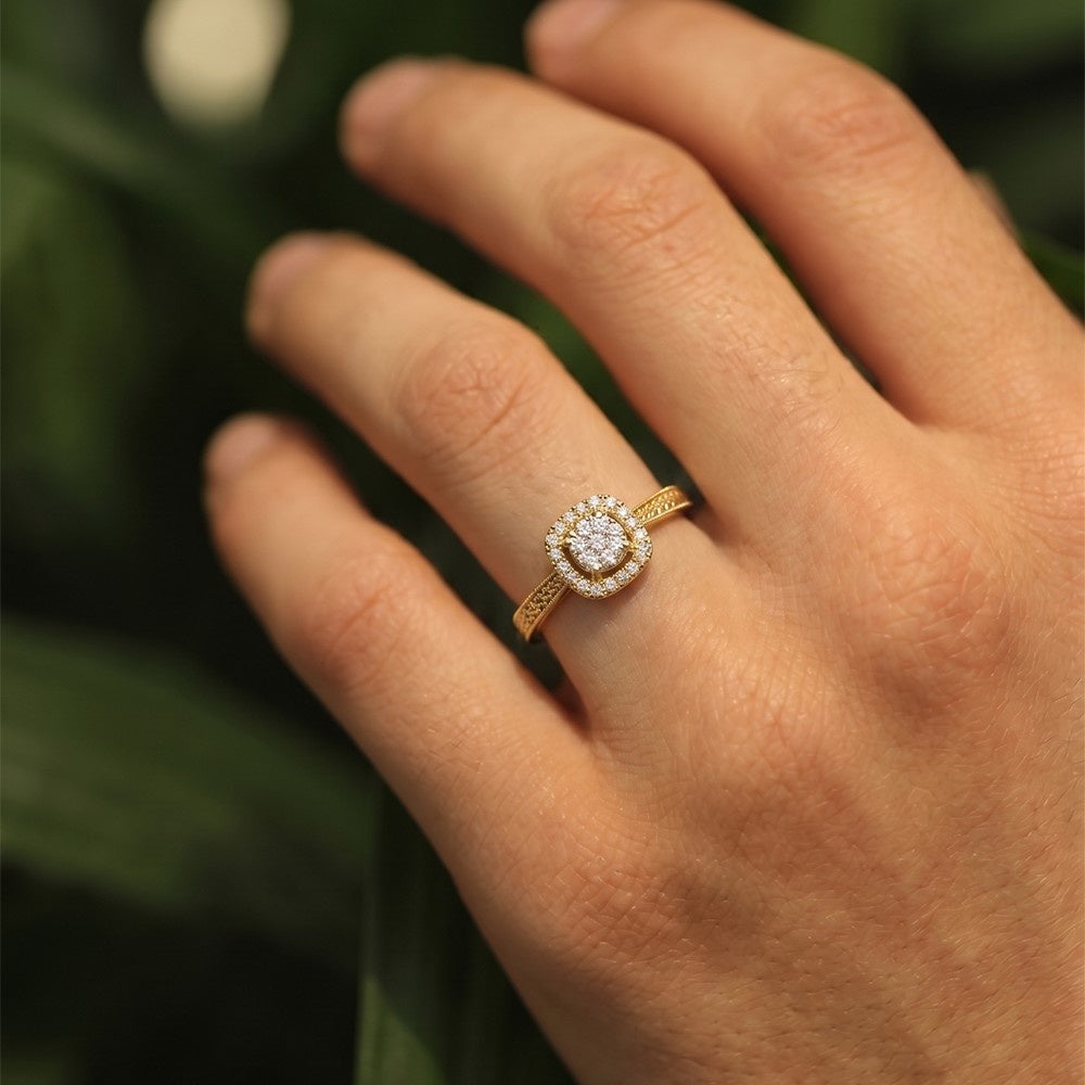 Gold ring with a diamond on a person's finger against a blurred green background
