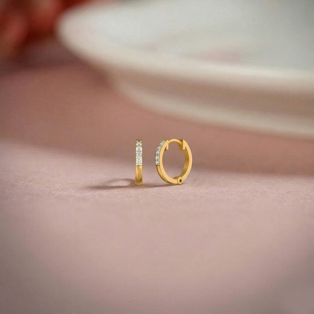 Gold and diamond hoop earring on a pink surface.