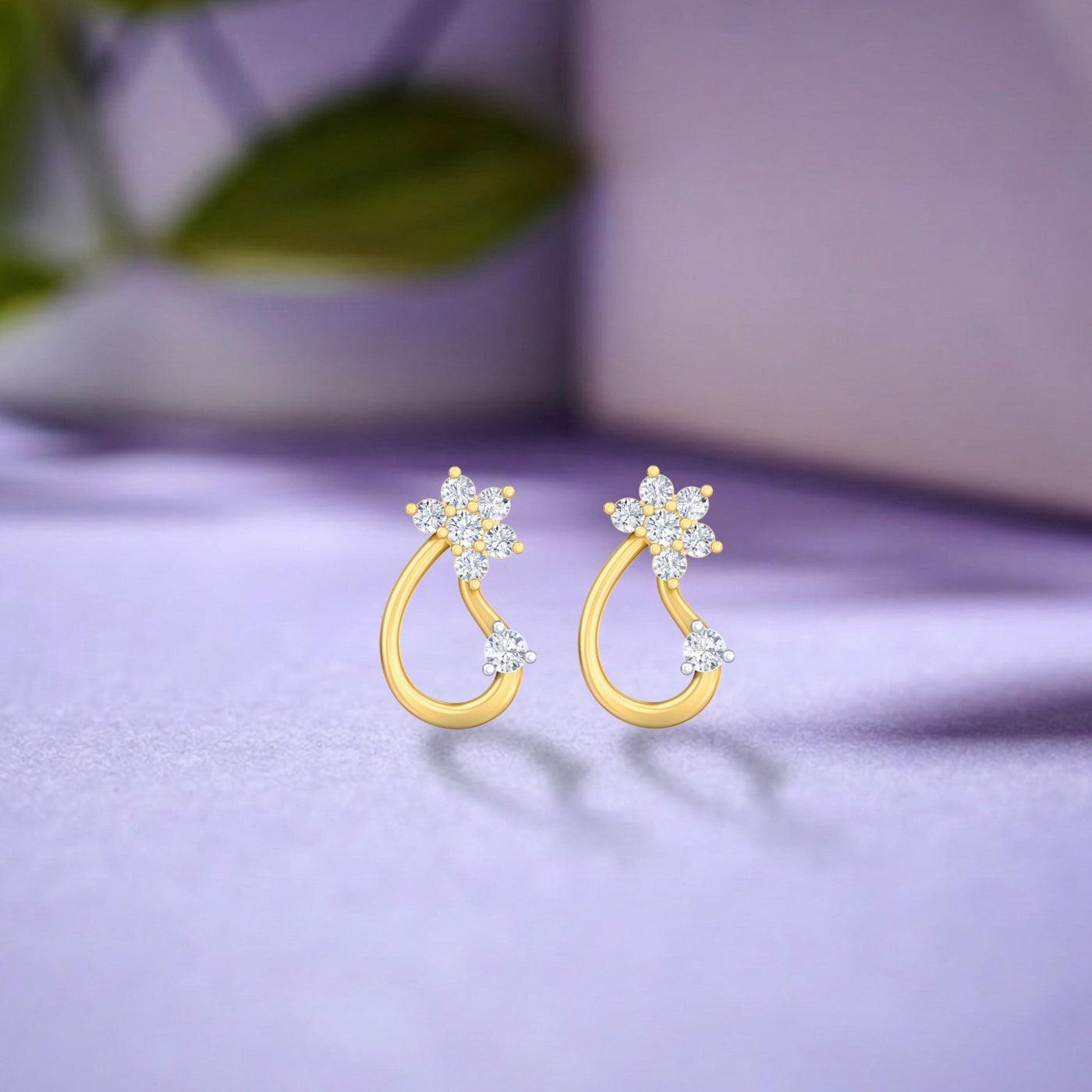 A pair of delicate yellow gold and diamond earrings resting on a soft lavender surface