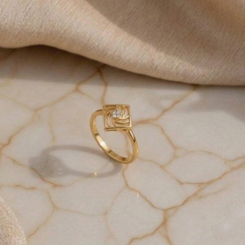 Gold ring with a diamond on a beige marble surface