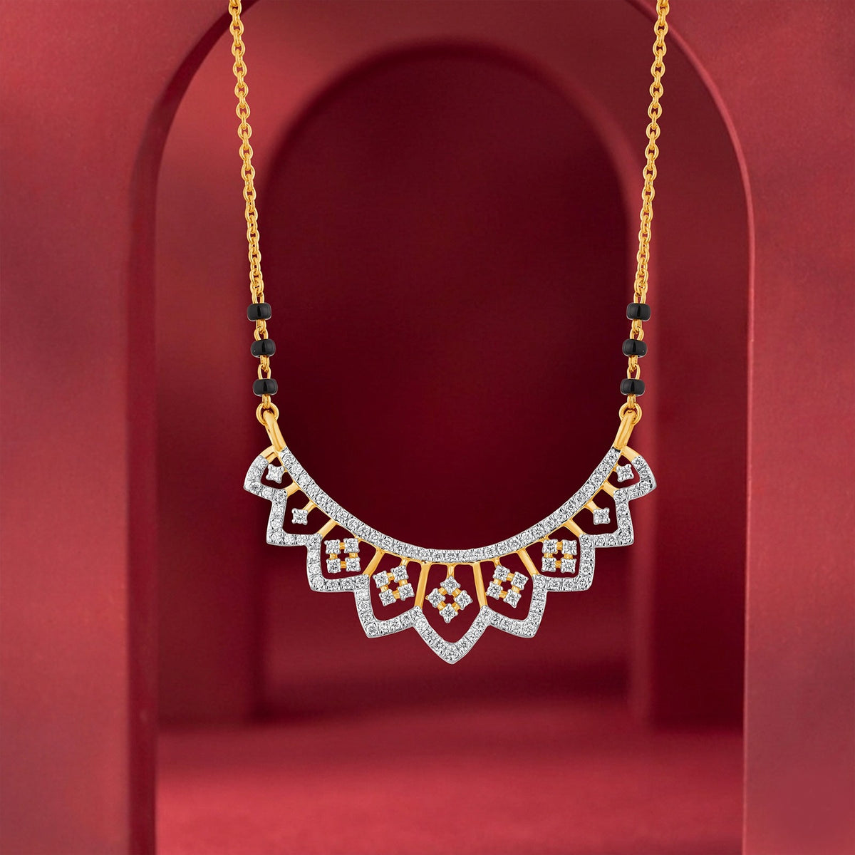 A gold mangalsutra with a semi-circular, scalloped paved with clear stones and accented with small red gemstone details, displayed against a dark red arched background.
