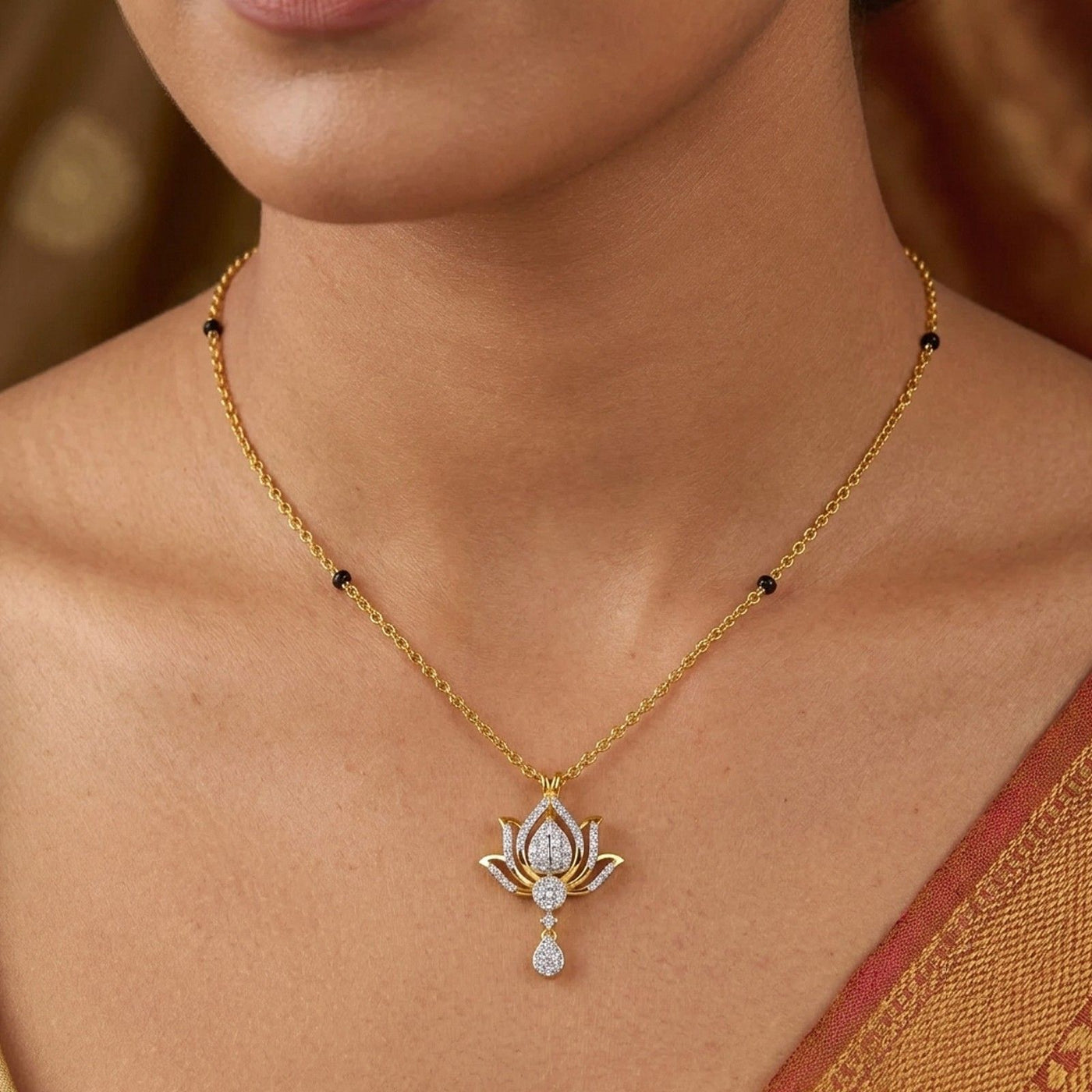 A close-up of a model wearing a delicate gold mangalsutra with a lotus-shaped pendant featuring clear gemstones and small black bead accents on the chain.